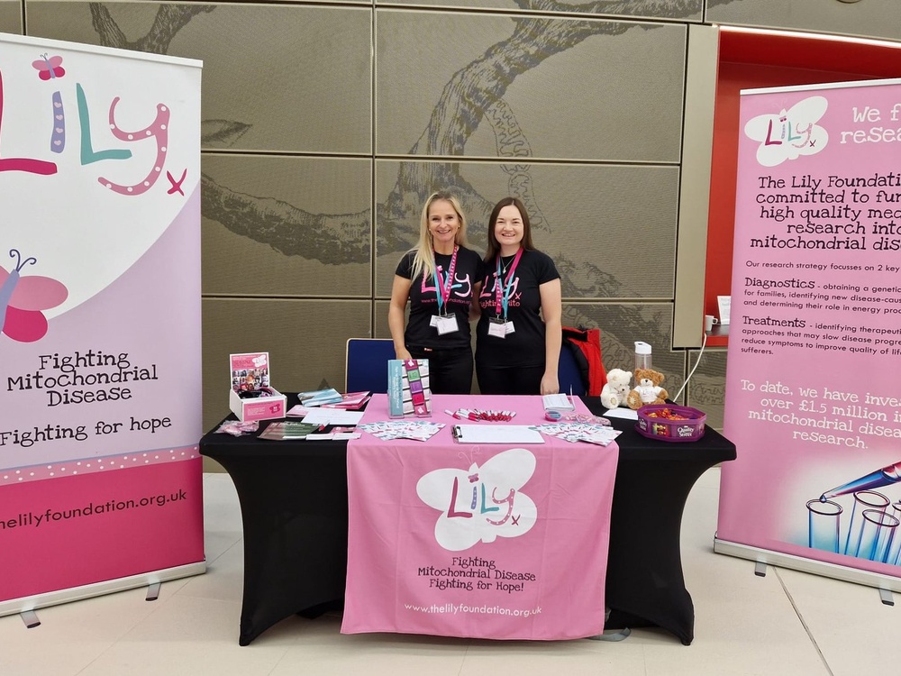 Two member of The Lily Foundation team stand next to each other behind an information stand covered in leaflets