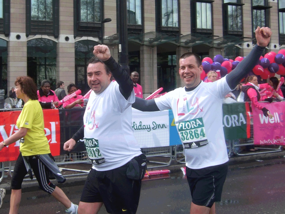 Two men in Lily Foundation white t-shirts run passed the camera with their arms triumphantly in the air