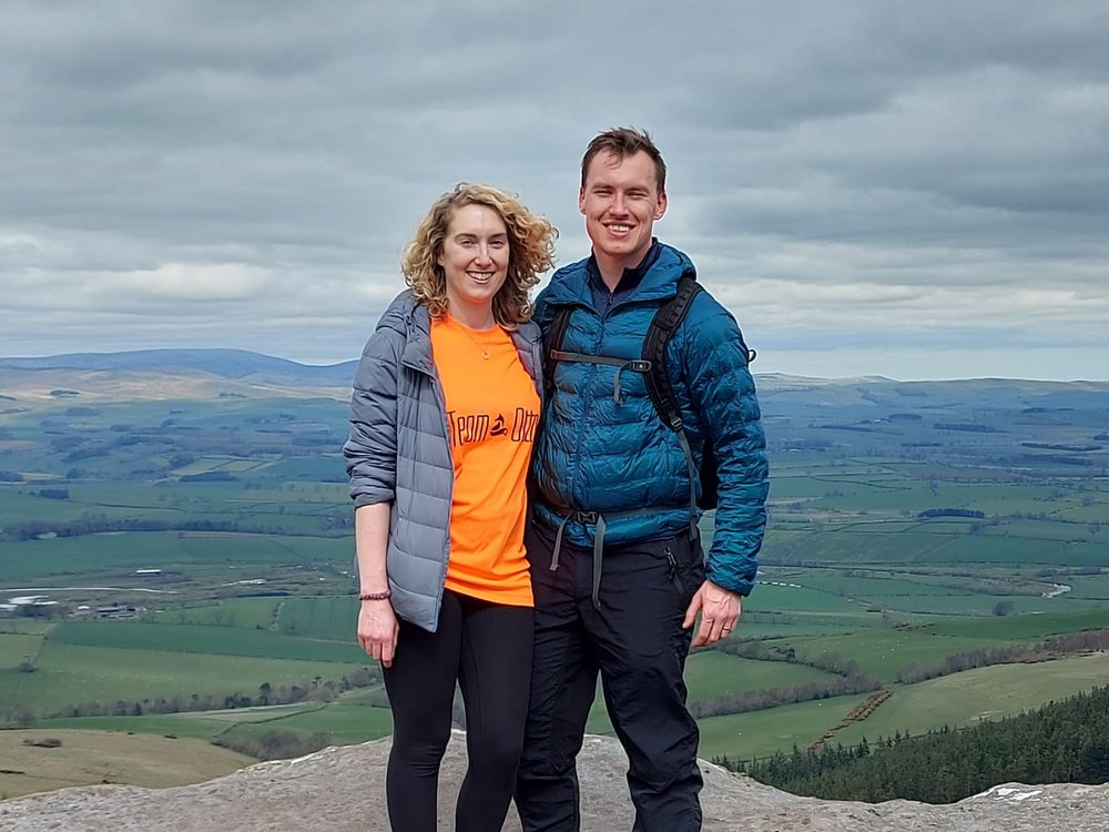 A woman and a man standing together on a hill with green fields behind them