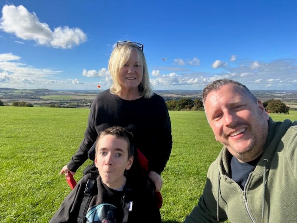 A boy with mitochondrial disease sitting in a wheelchair with his parents