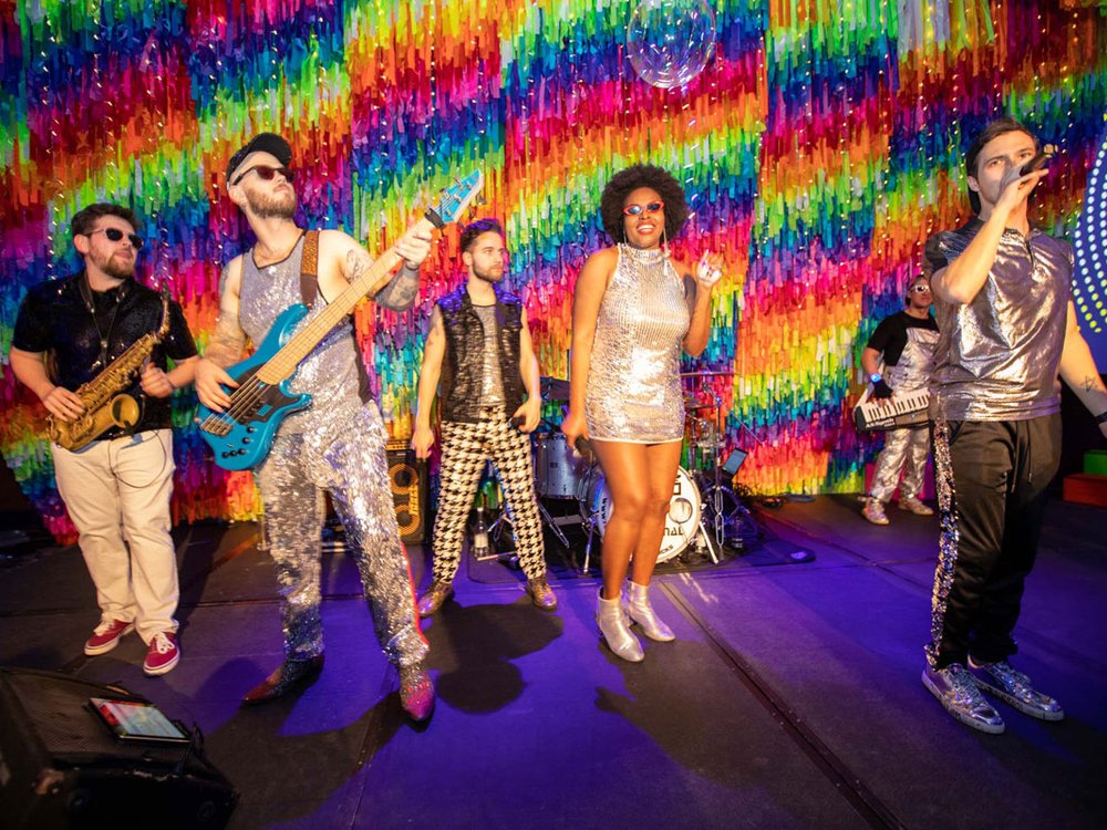 Lily Foundation Charity Ball - live band singing against a mutli-coloured rainbow ribbon backdrop