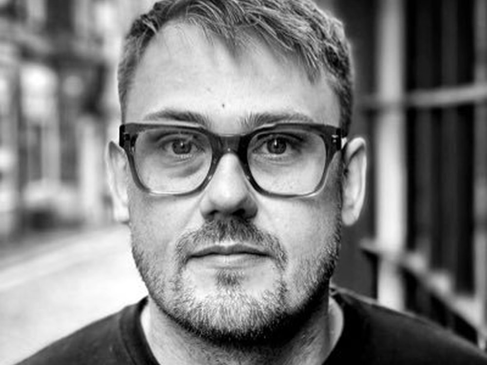 Close-up black and white of a man in glasses standing in a street