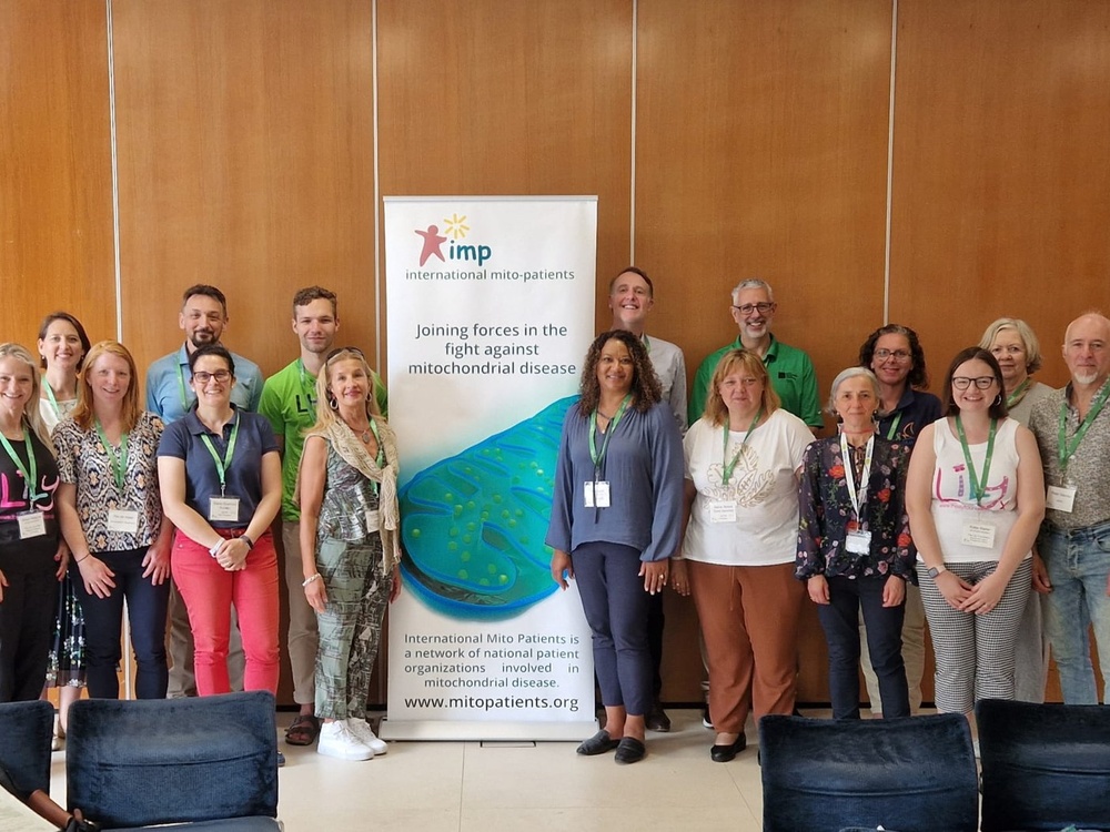 A group of people smiling and standing around a large banner for International Mito Patients