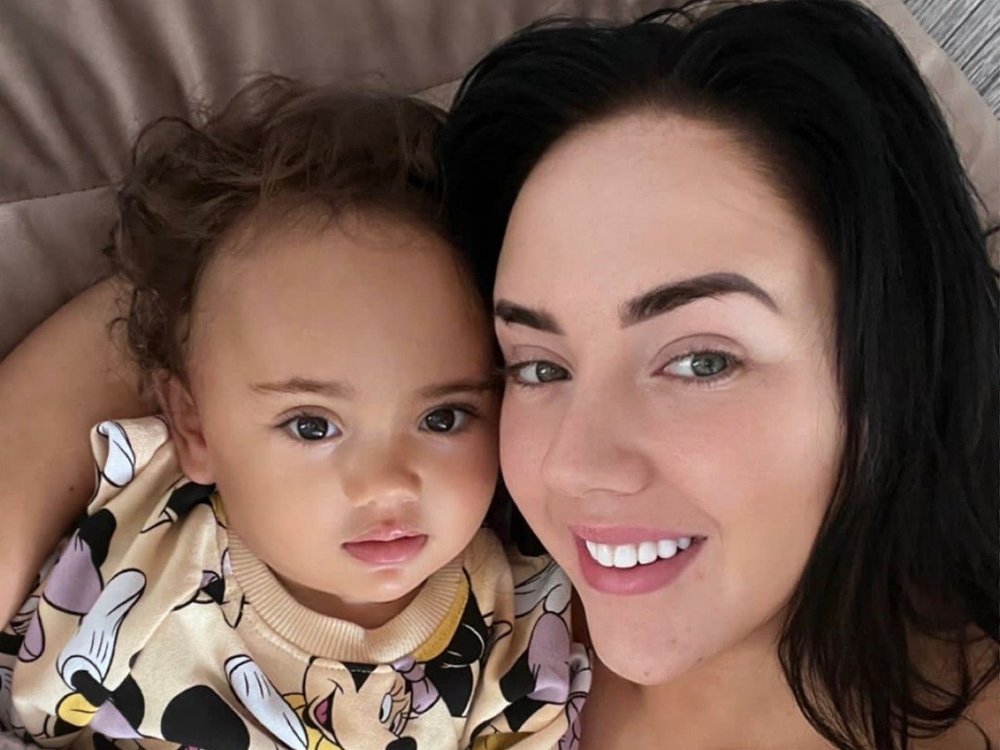 A young women hold a baby, both looking at the camera and the woman is smiling