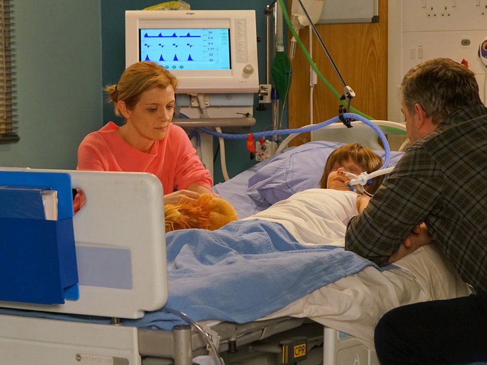 two men and a woman sit around a hospital bed. In it is a little boy asleep connecting to a breathing tube