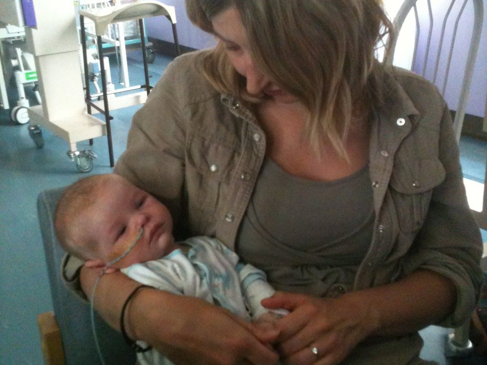 A lady sits in a chair cradling a small baby in a hospital room