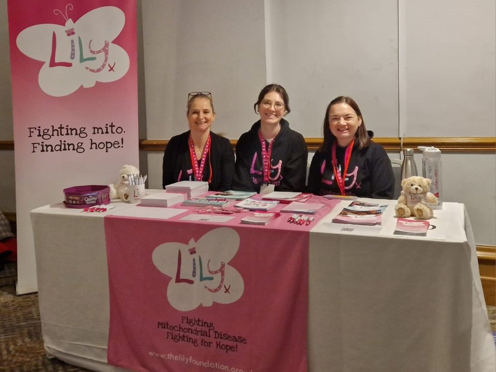 Three members of Lily staff sit at an awareness table covered in Lily Foundation leaflets