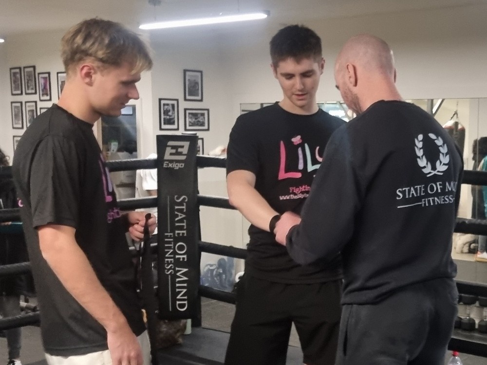 Two boxers in Lily tops standing in the ring with a trainer