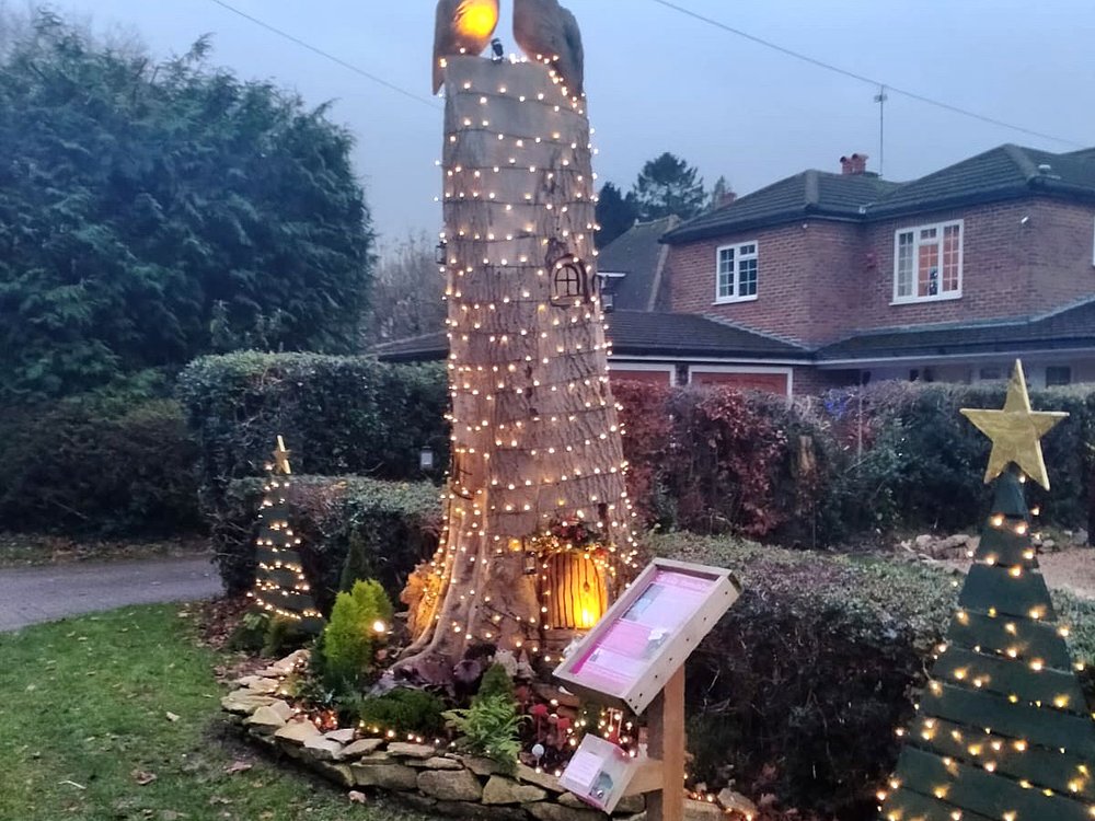 An old tree trunk outside someones house, decorated to look like a magical tree, with owls and fairy lights all around it