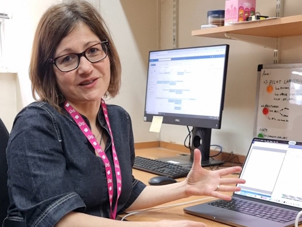 A lady wearing a Lily lanyard sitting at a desk with a laptop in front of her