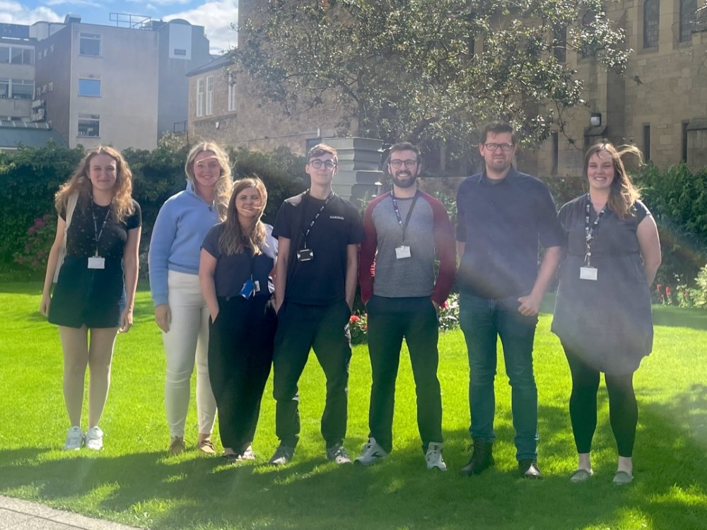 A group of people standing side by side on a lawn outside a building