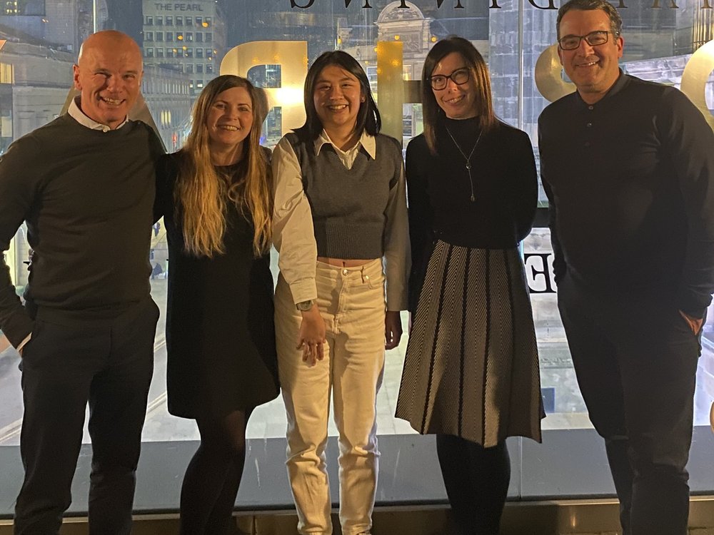 A group of five people standing in a restaurant window with a cityscape behind