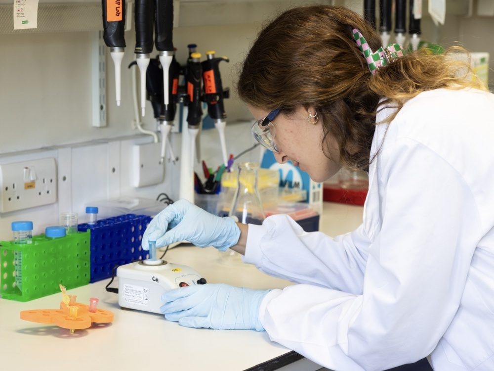 A lady in a white coat leaning over a counter using medical equipment