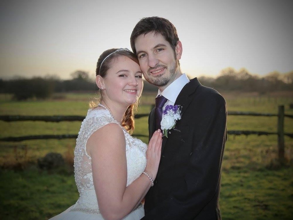 Josey in her wedding dress and her husband Chris in suit, tie and buttonhole standing cheek-to-cheek