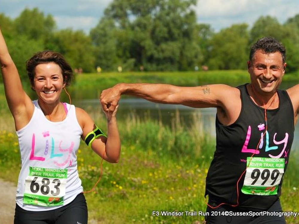 A women in a white Lily running vest runs next to a man in a black lily running vest