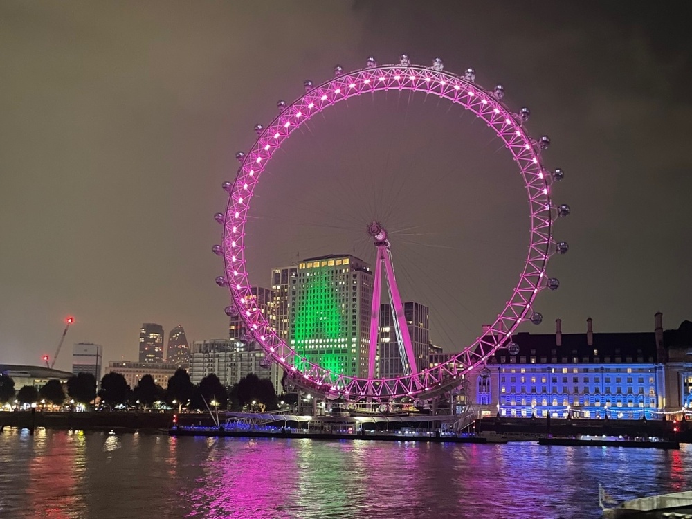 The Shell Centre and London Eye lit up green at night with the Thames in the foreground