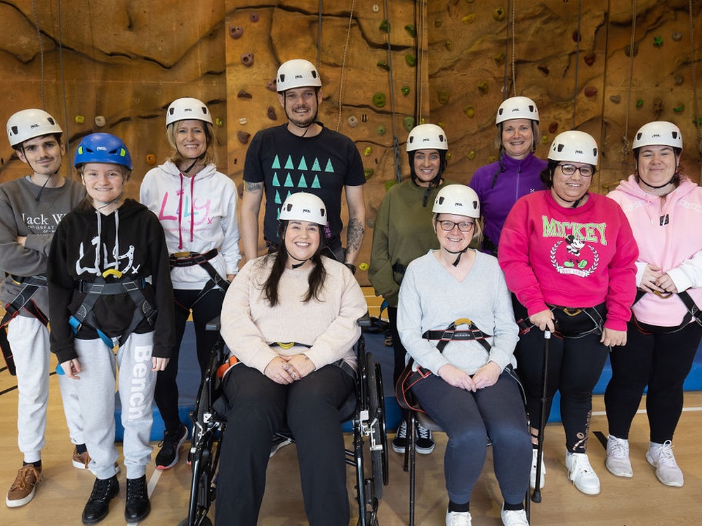 A group of people wearing protective headgear and harnesses in front of a climbing wall