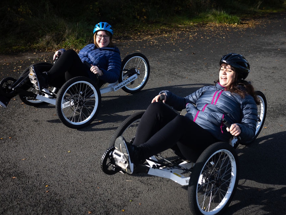 Two ladies with cycle helmets on laughing and riding recumbent bikes