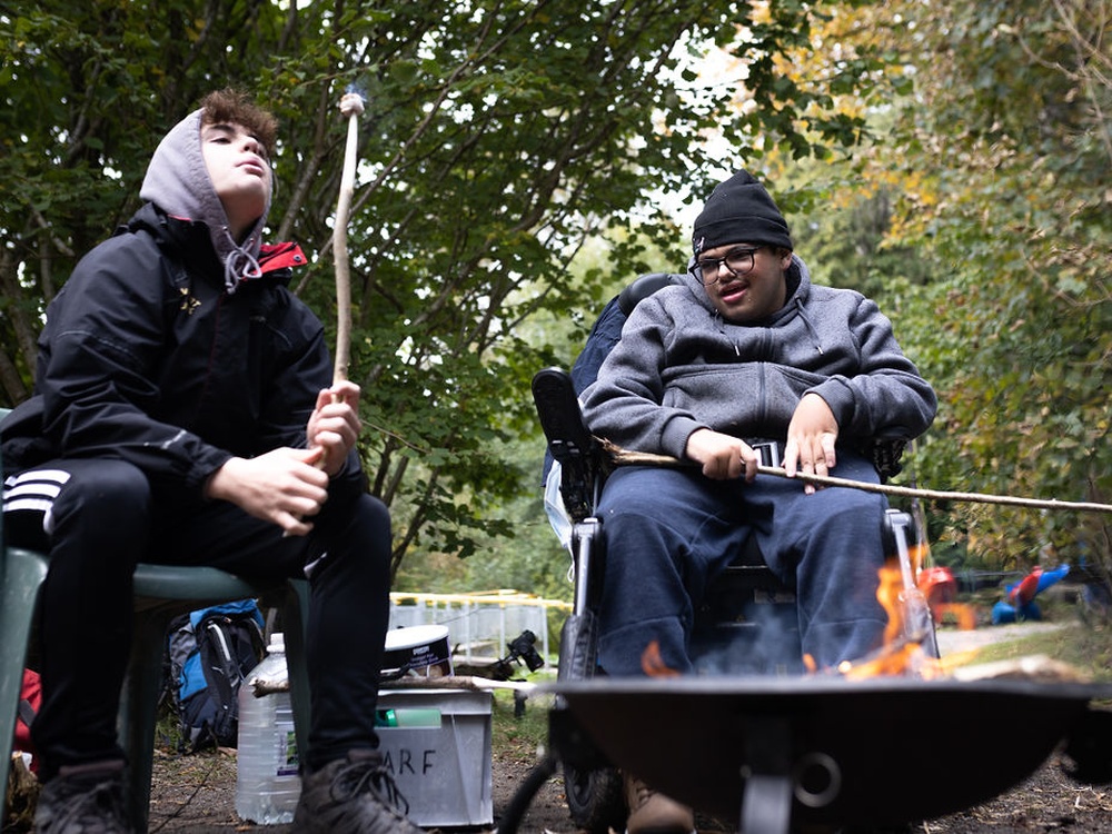 Two young adult mito patients toasting marshmallows around a campfire