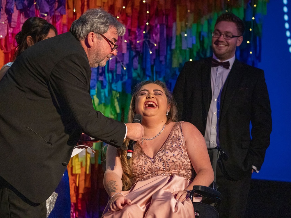 A young adult mito patient laughing on stage at the Lily ball