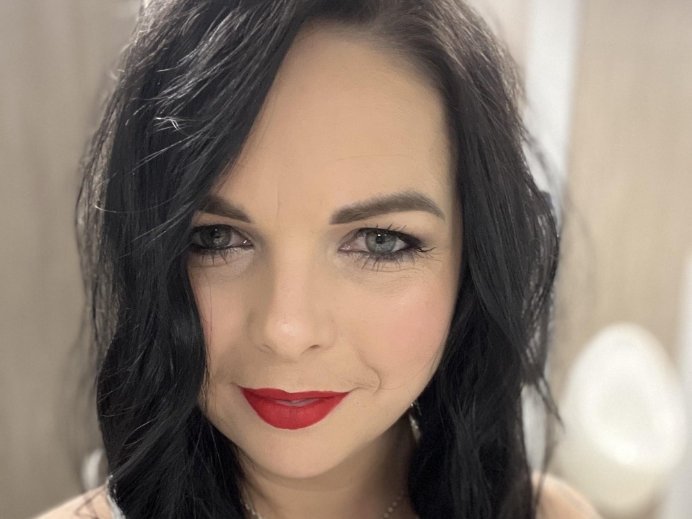 A headshot of a woman with long dark hair smiles to the camera