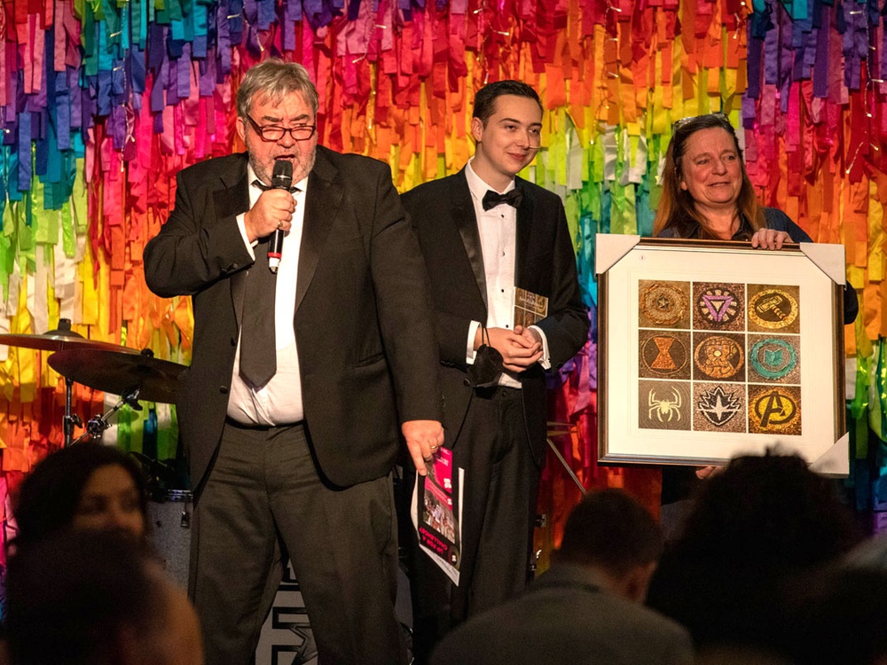 Presenters on stage running a charity auction and holding a picture