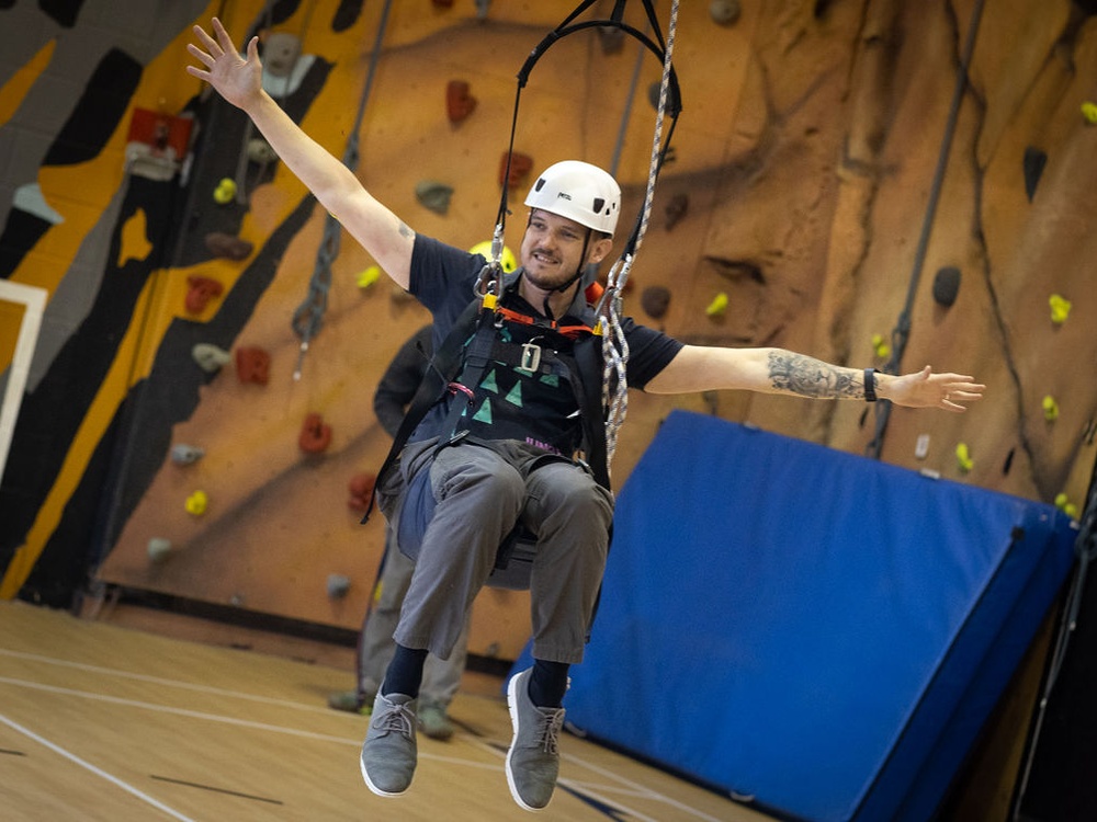 A man harnessed into a large swing smiling with his hands raised in the air