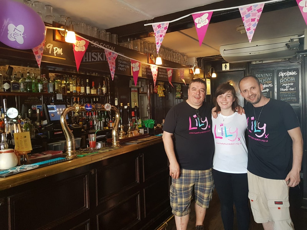 Three people in Lily tops standing at the bar in a pub