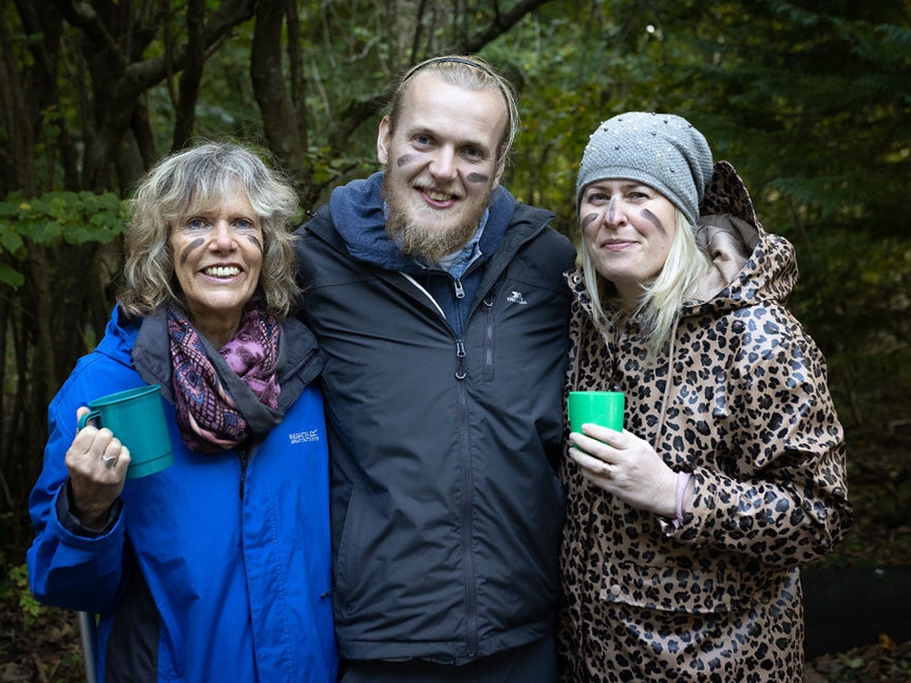 Three people outside with their faces painted black and their arms around one another