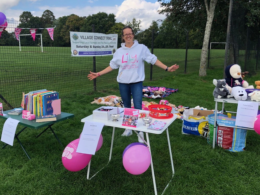 A lady standing behind a table set with Lily Foundation balloons and leaflets