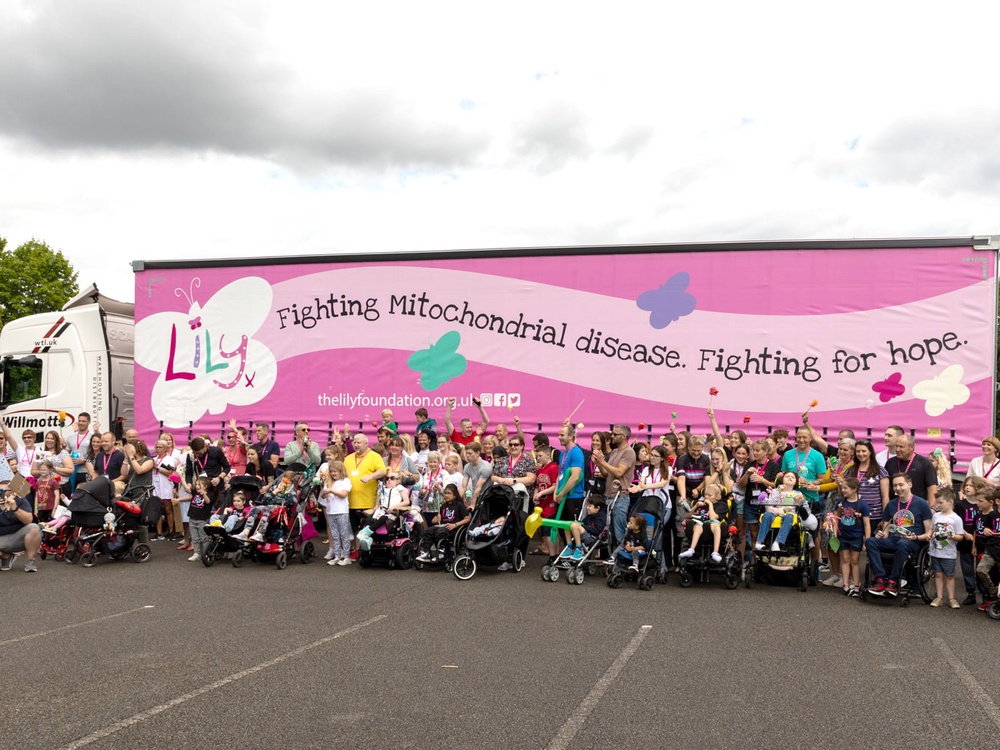 A large group of people standing at the side of a huge lorry with a Lily Foundation livery