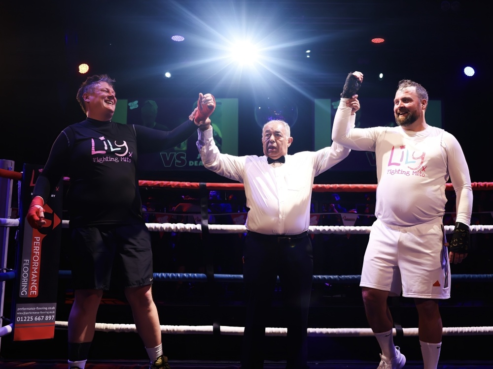 A referee holding up the arms of two boxers at the Lily Fight Night