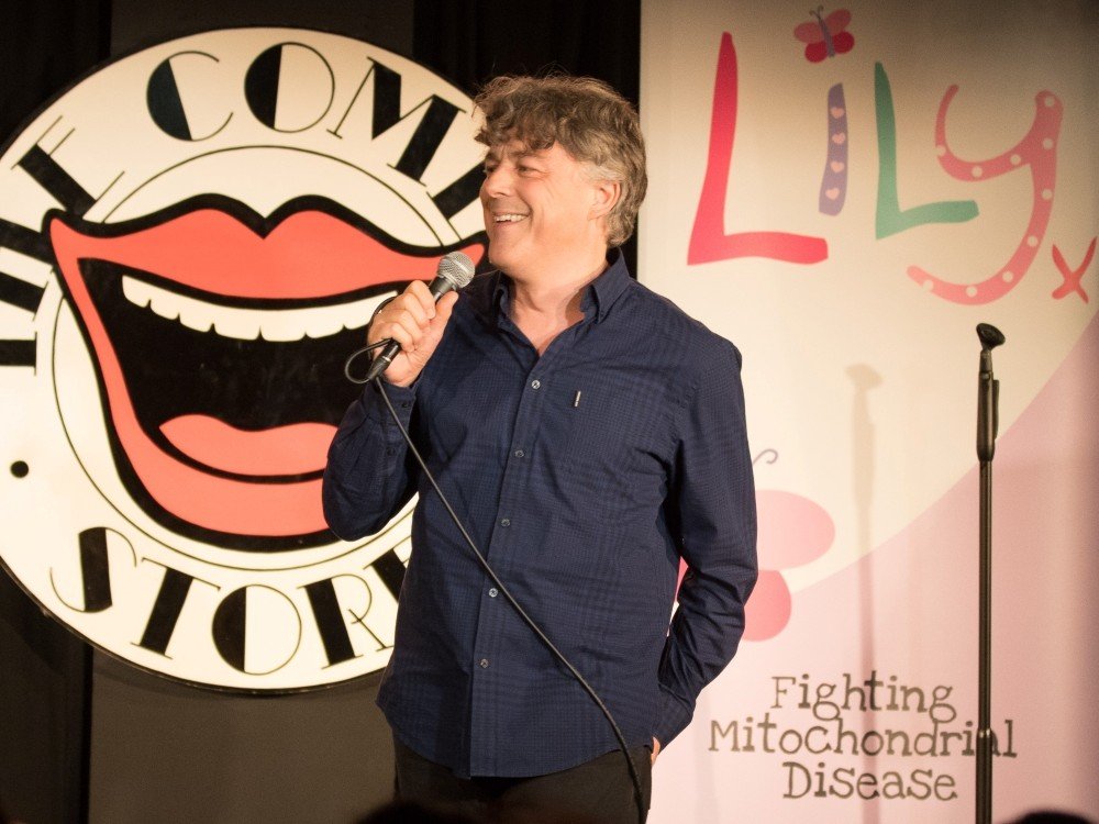 Let’s make 2025 a year to remember! - Comedian Alan Davies on stage with a mic at The Lily Foundation Comedy Night