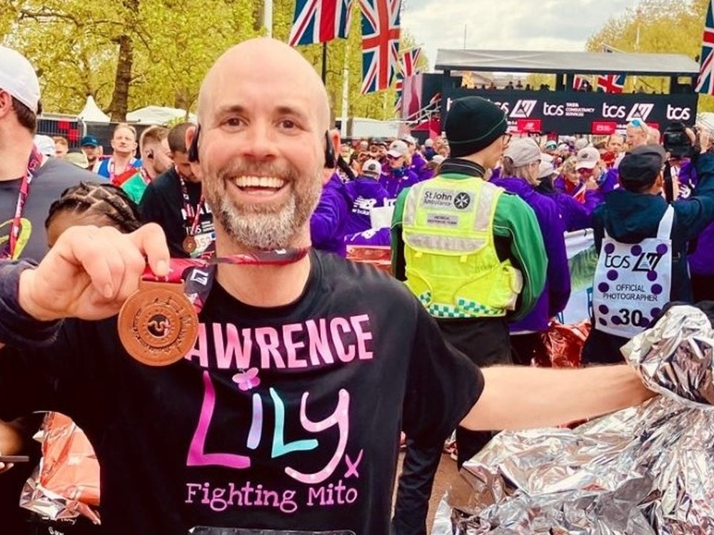 Marathon effort to fight mito - A man in a Lily Foundation t-shirt smiling and holding up his London Marathon finishers medal